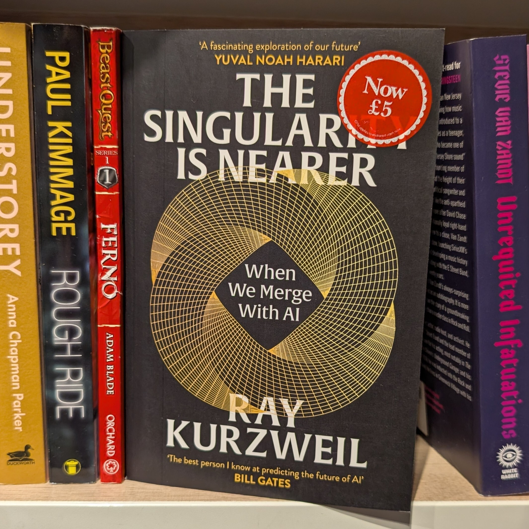 Book titled 'The Singularity Is Nearer: When We Merge With AI' by Ray Kurzweil, with a price sticker of £5, is displayed among other books on a shelf at Foyles.
